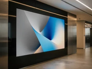 Groot digitaal beeldscherm met levendige merkvisuals op een grijze kantoormuur, verlicht door warm omgevingslicht in een moderne bedrijfsgang.