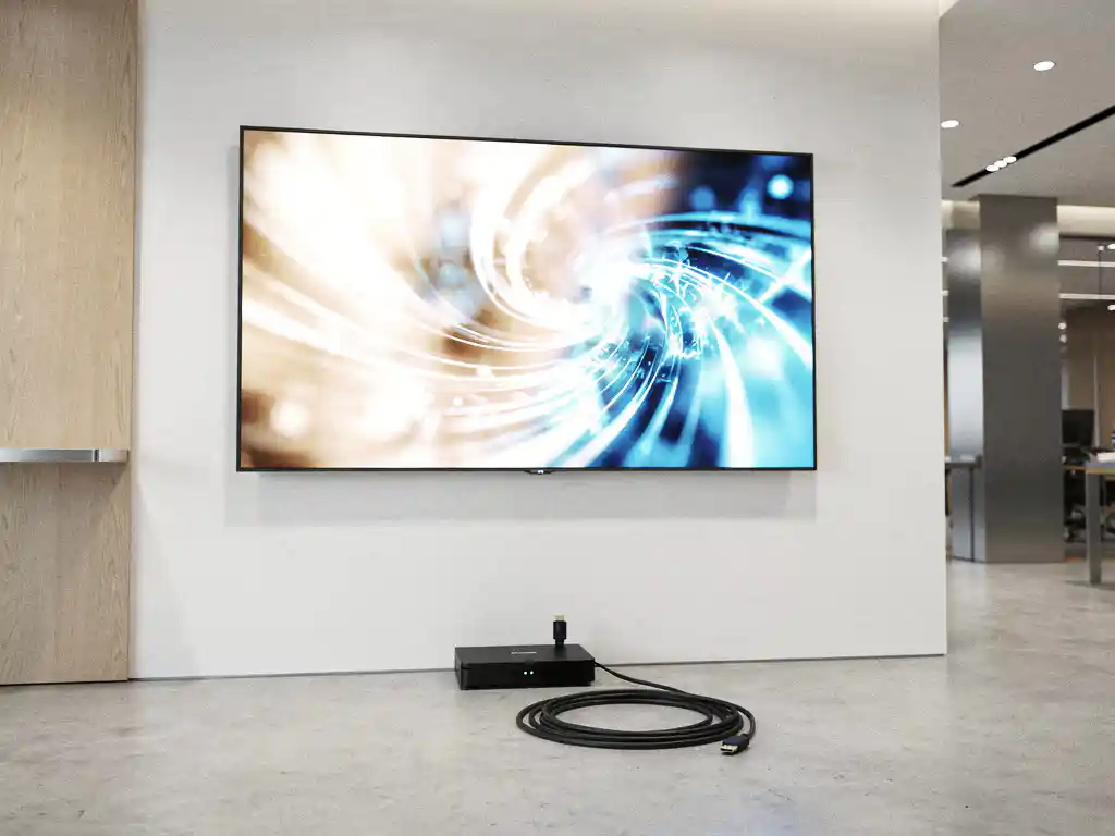 Groot digitaal beeldscherm aan witte wand in moderne lobby, met mediaspeler en HDMI-kabel op de vloer eronder.